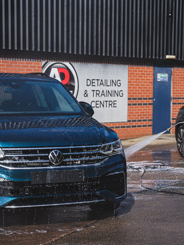 Trainee rinsing off a car during course in front of the "AD Detailing and Training Centre" sign