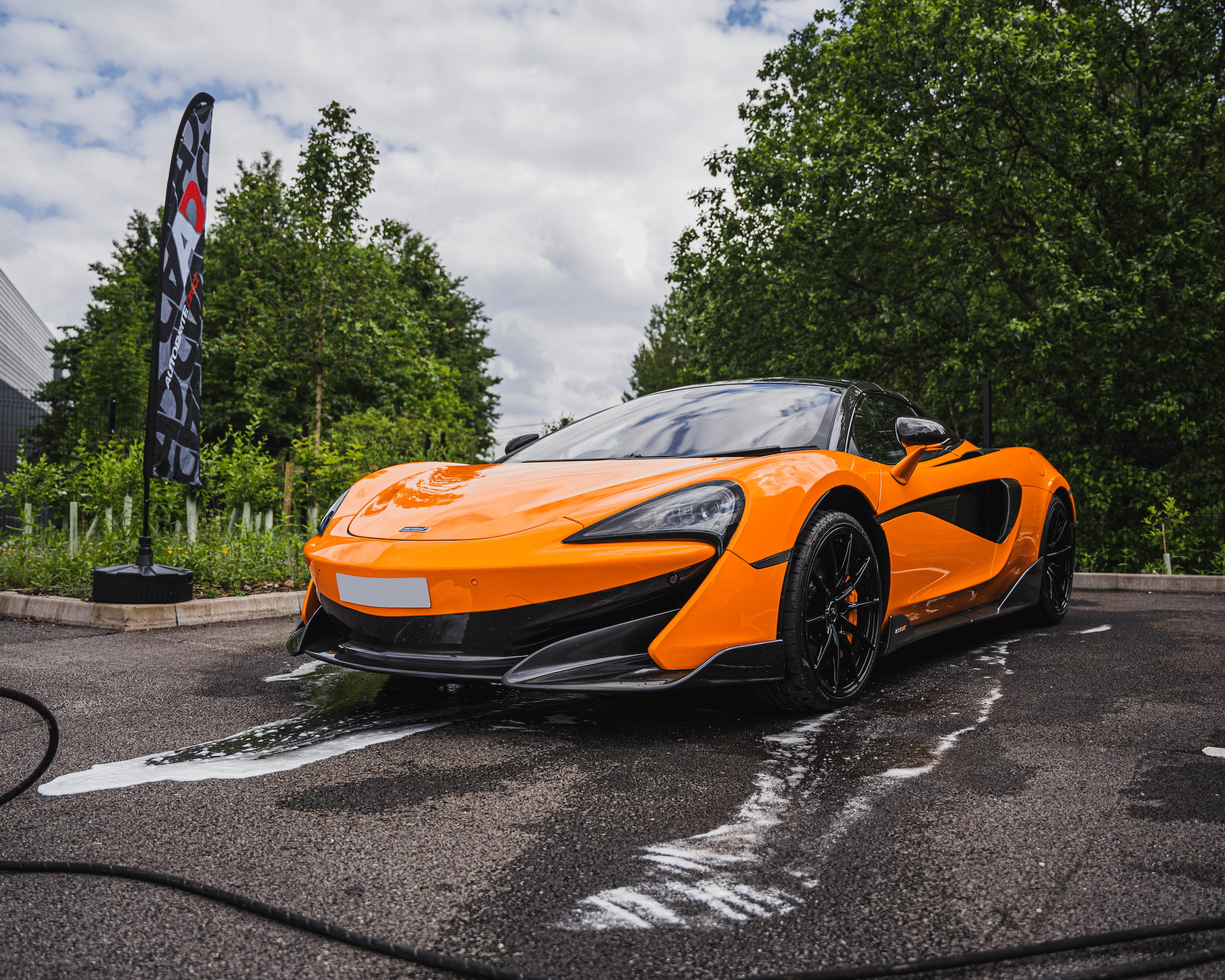 Orange Mclaren being cleaned with a AD flagpole in the background