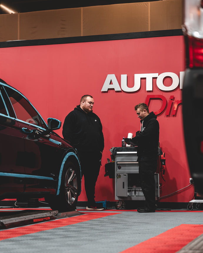 Nath and a trainee next to the Autobrite Direct sign and a taped up car ready to be detailed